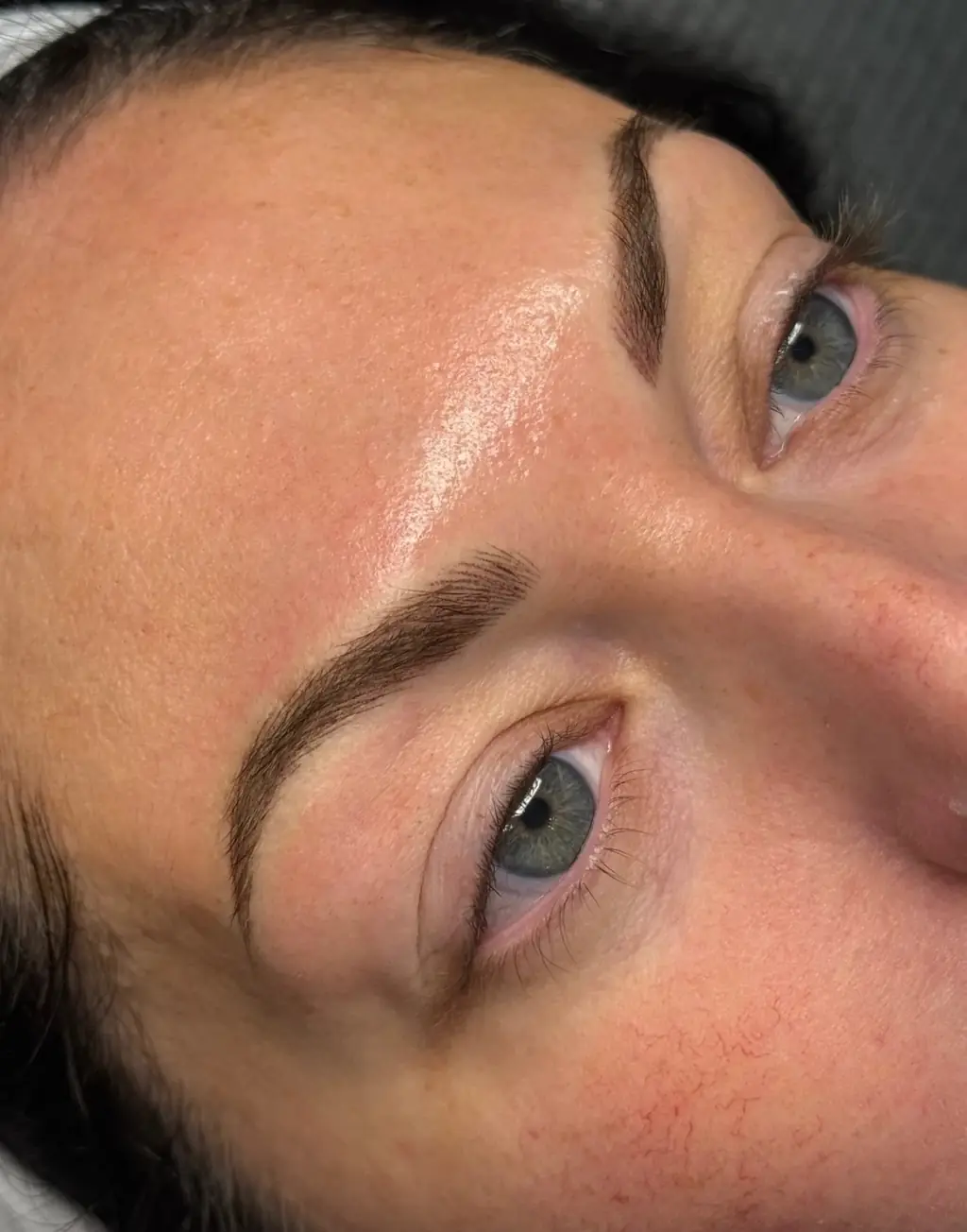 Close-up of a client's freshly done brows: full, softly defined hair-like strokes above blue-grey eyes